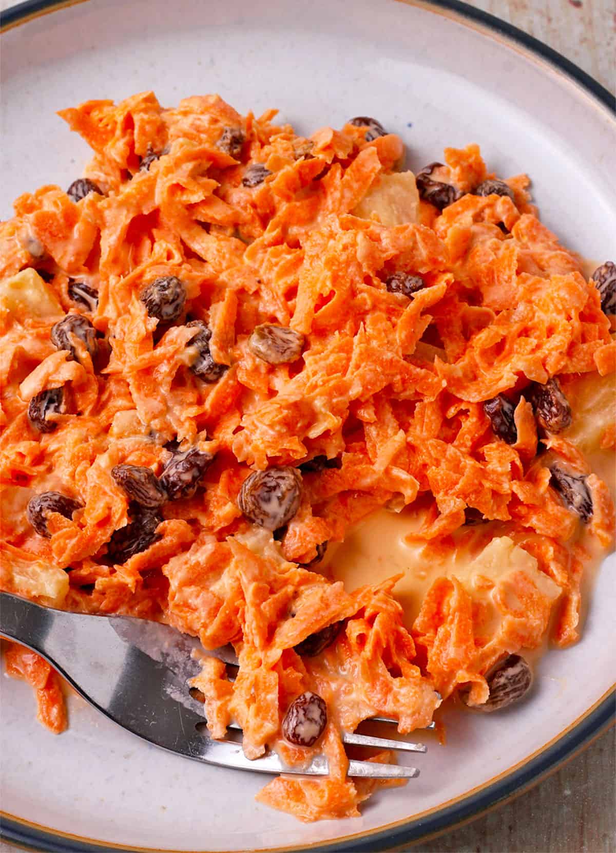 Carrot, raisin, pineapple salad on a plate with a fork.