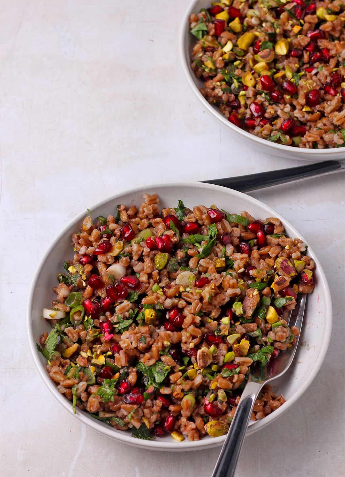 Two small bowls of farro pomegranate salad with forks in the bowl.