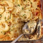 Vegan scalloped potatoes with chives and a spoon in the baking dish.