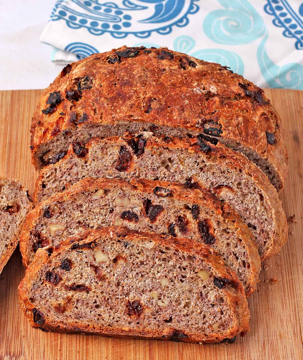 Cranberry walnut bread is sliced on a board with the loaf behind the slices.