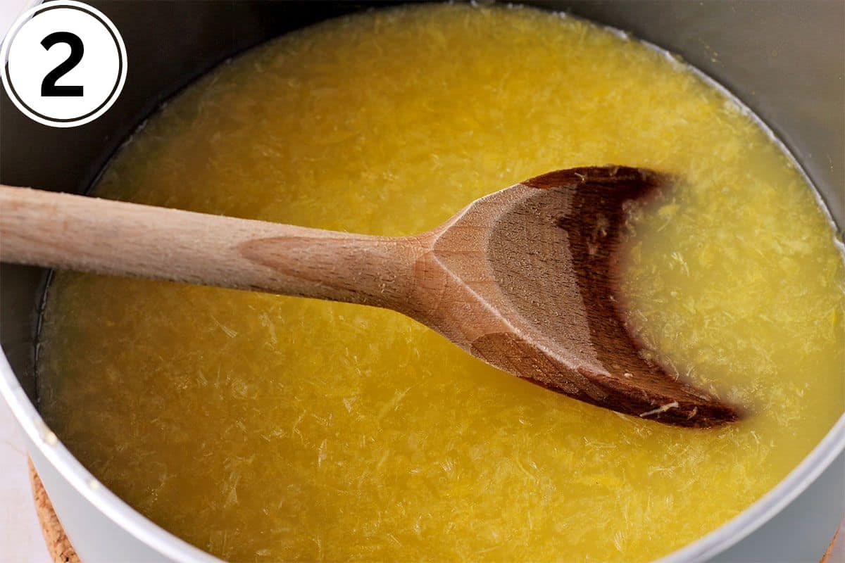 Orange juice is stirred in a saucepan with a wooden spoon.