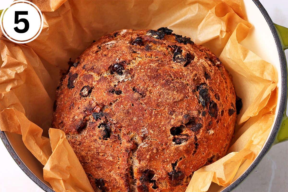 Baked cranberry walnut bread in parchment paper in a Dutch oven.