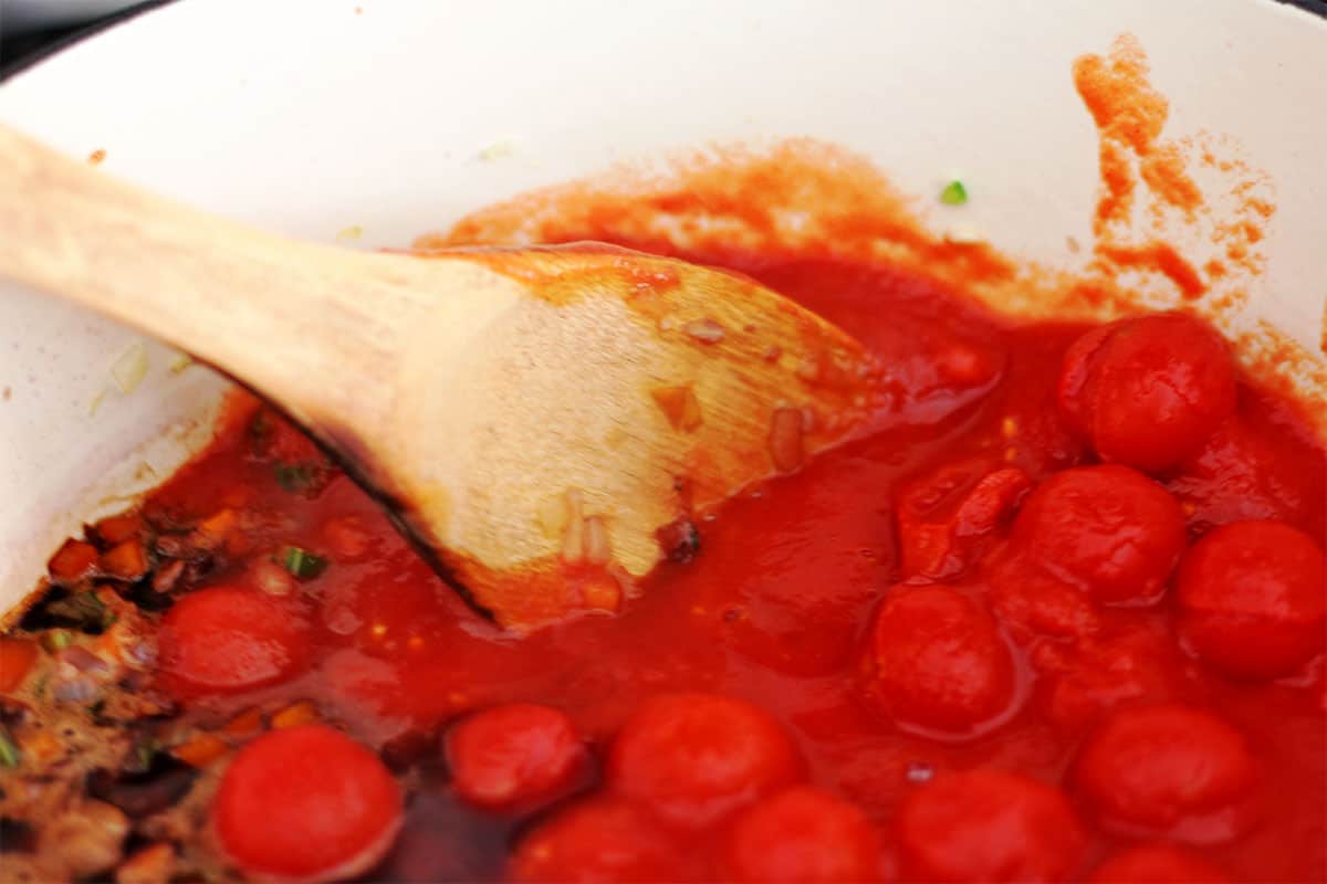 Canned cherry tomatoes are stirred in a pot.