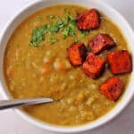 Vegan split pea soup in a white bowl with a spoon. Smoked tofu and parley tops the soup.