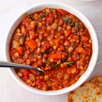A bowl of vegetable barley and lentil soup with a spoon.