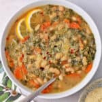 A bowl of Tuscan white bean soup with a spoon and vegan parmesan on top.