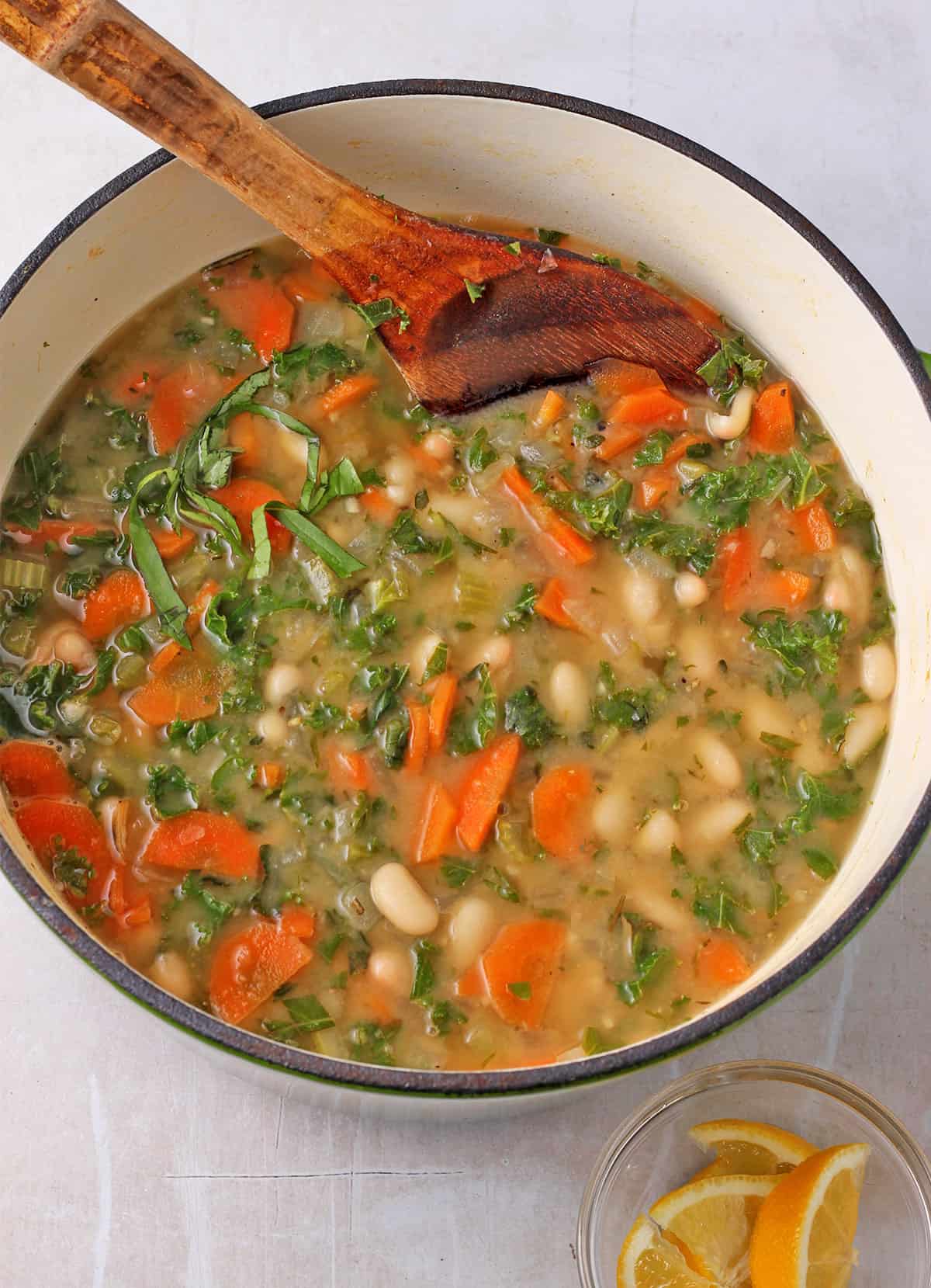 A pot of white bean soup with vegetables, herbs, and kale.