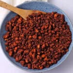 A blue bowl of tofu chorizo sausage crumbles with a wooden spoon.