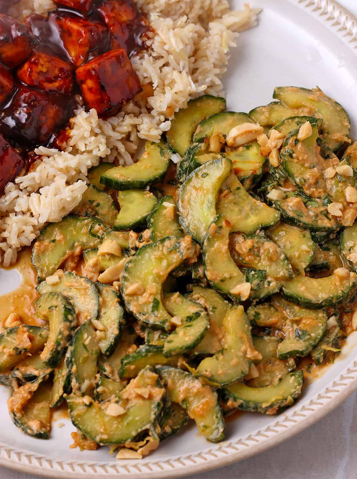 Creamy cucumber salad on a plate with BBQ tofu and rice.