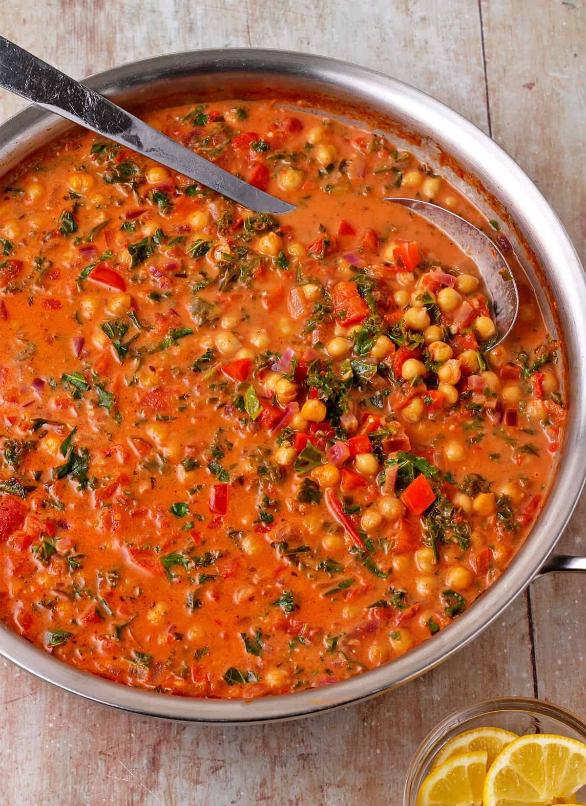 Chickpeas and kale in tomato and harissa sauce in a pan with a spoon.