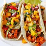 Tempeh asada tacos with mango salsa and lettuce on a white plate.