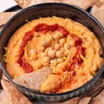 A pita chip is dipped into a bowl of harissa hummus.