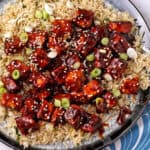 Korean BBQ tofu on a plate over rice with sesame seeds and green onions.