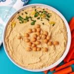 A bowl of hummus with chickpeas, lemon zest, and chopped parsley on top.