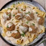 A plate of vegan Swedish meatballs with sour cream gravy over wide noodles.