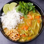 A bowl of massaman curry with potatoes, carrots, green beans topped with rice, peanuts, and cilantro.