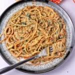 Vegan sundried tomato pasta with bacon bits is on a plate with a fork wrapped around some of the spaghetti.