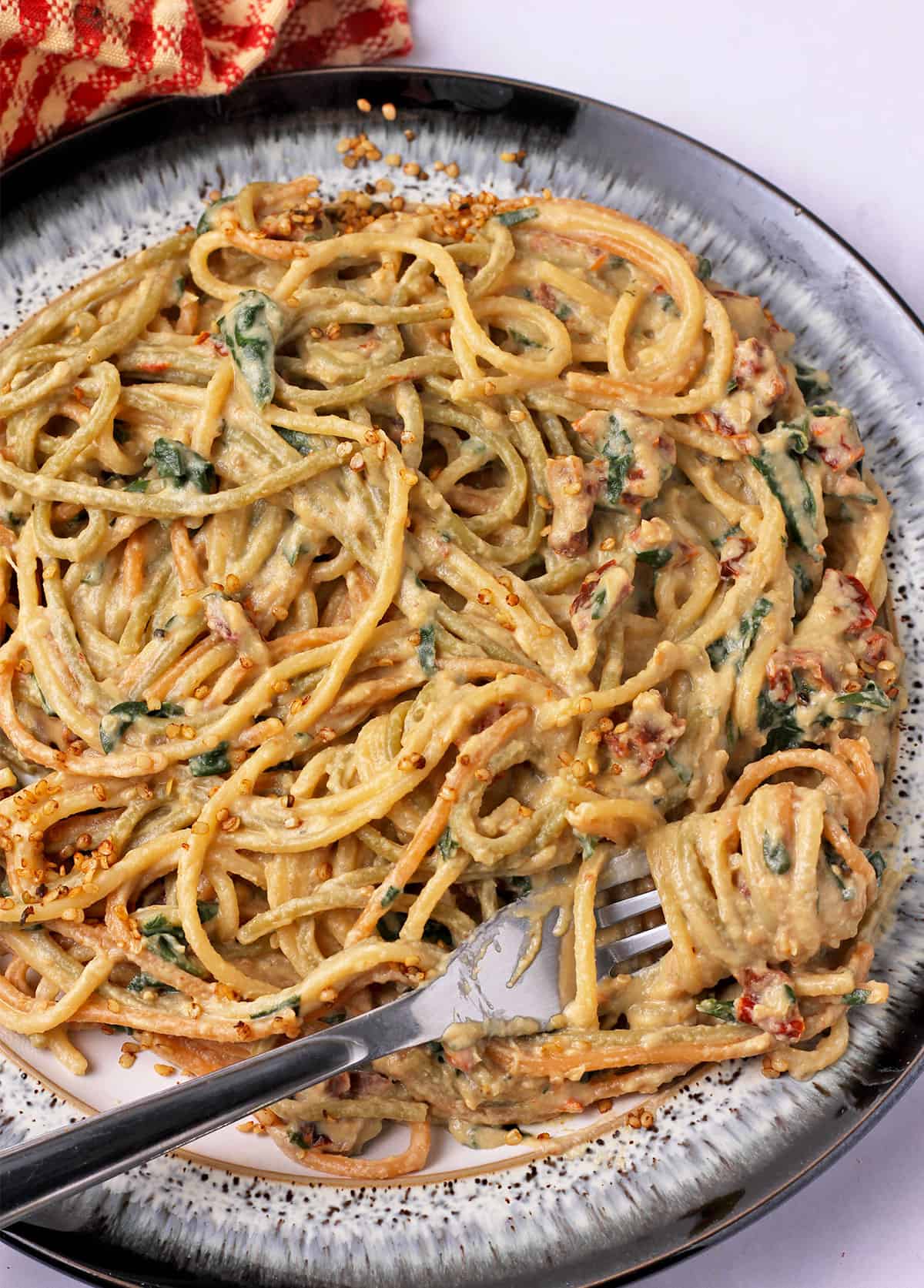 A plate of sundried tomato pasta with spaghetti and a fork wrapped around the pasta.