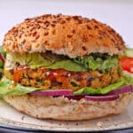 Close up of veggie burger in a bun with mango chutney, lettuce, tomatoes, and onions.