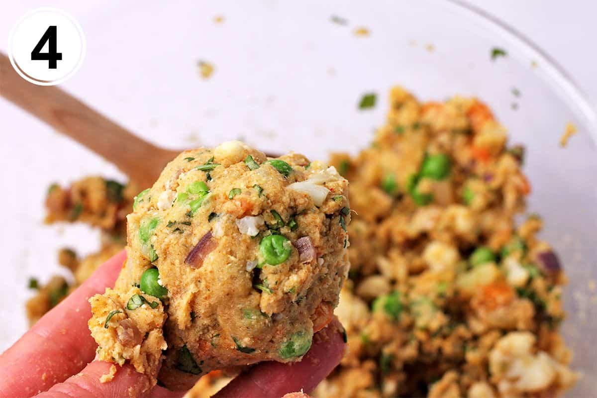 A hands holds a ball of veggie burger mixture with potatoes, peas, onions, and cilantro.