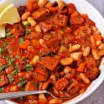 A bowl of white bean stew with smoky tofu garnished with parsley and lemon wedges.