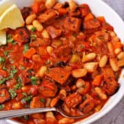 A bowl of white bean stew with smoky tofu garnished with parsley and lemon wedges.