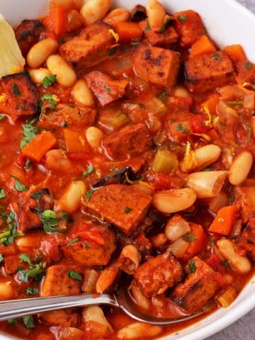 A bowl of white bean stew with smoky tofu garnished with parsley and lemon wedges.