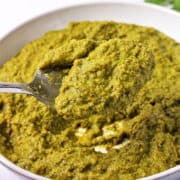A spoonful of Thai green curry paste held over a bowl of paste.
