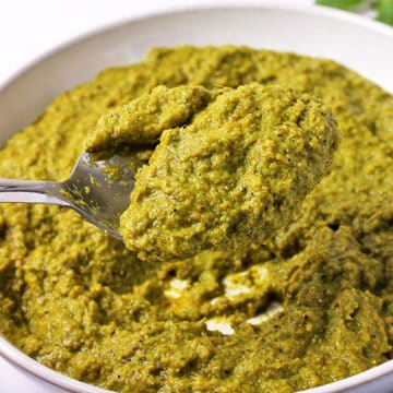 A spoonful of Thai green curry paste held over a bowl of paste.