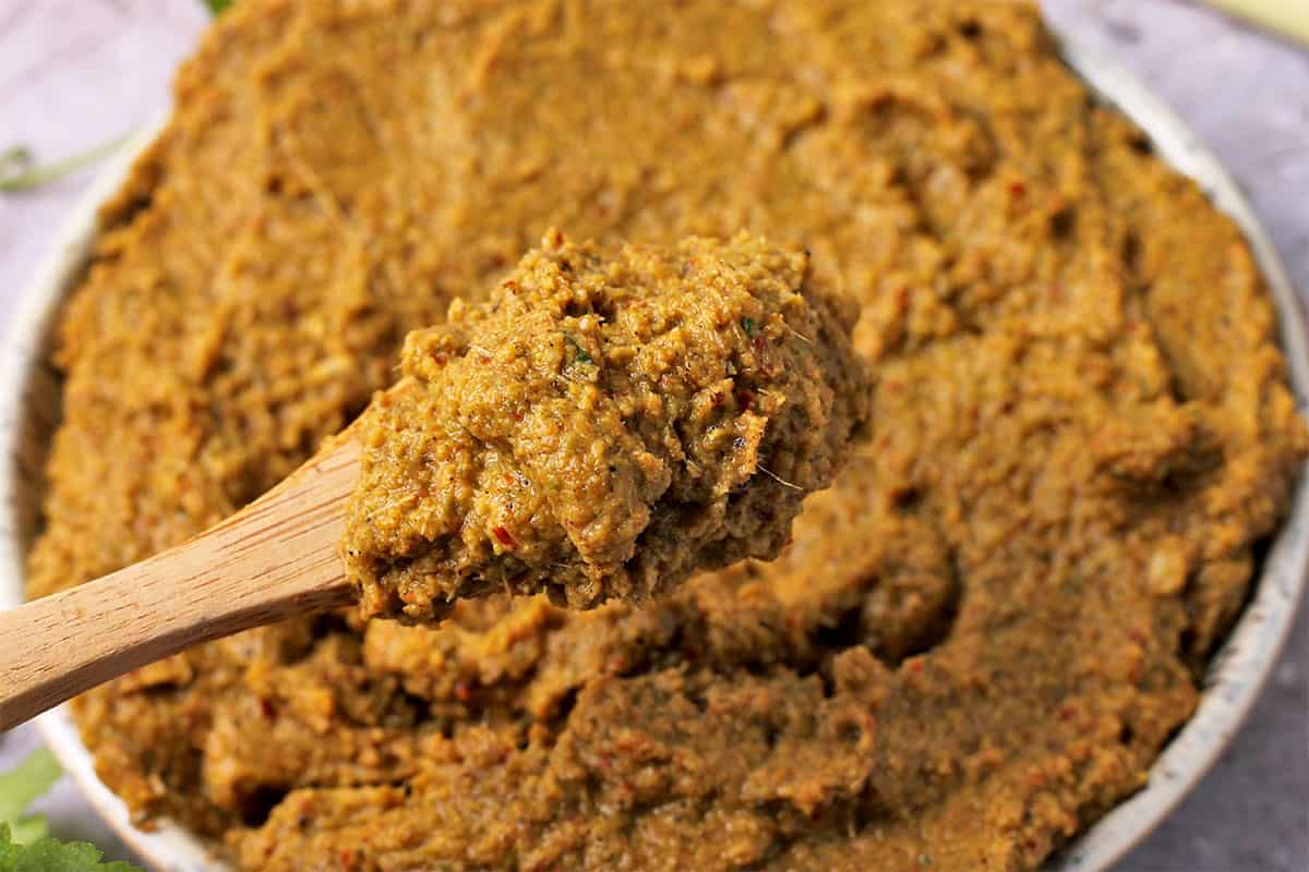 A wooden spoonful of massaman curry lifted above a bowl.