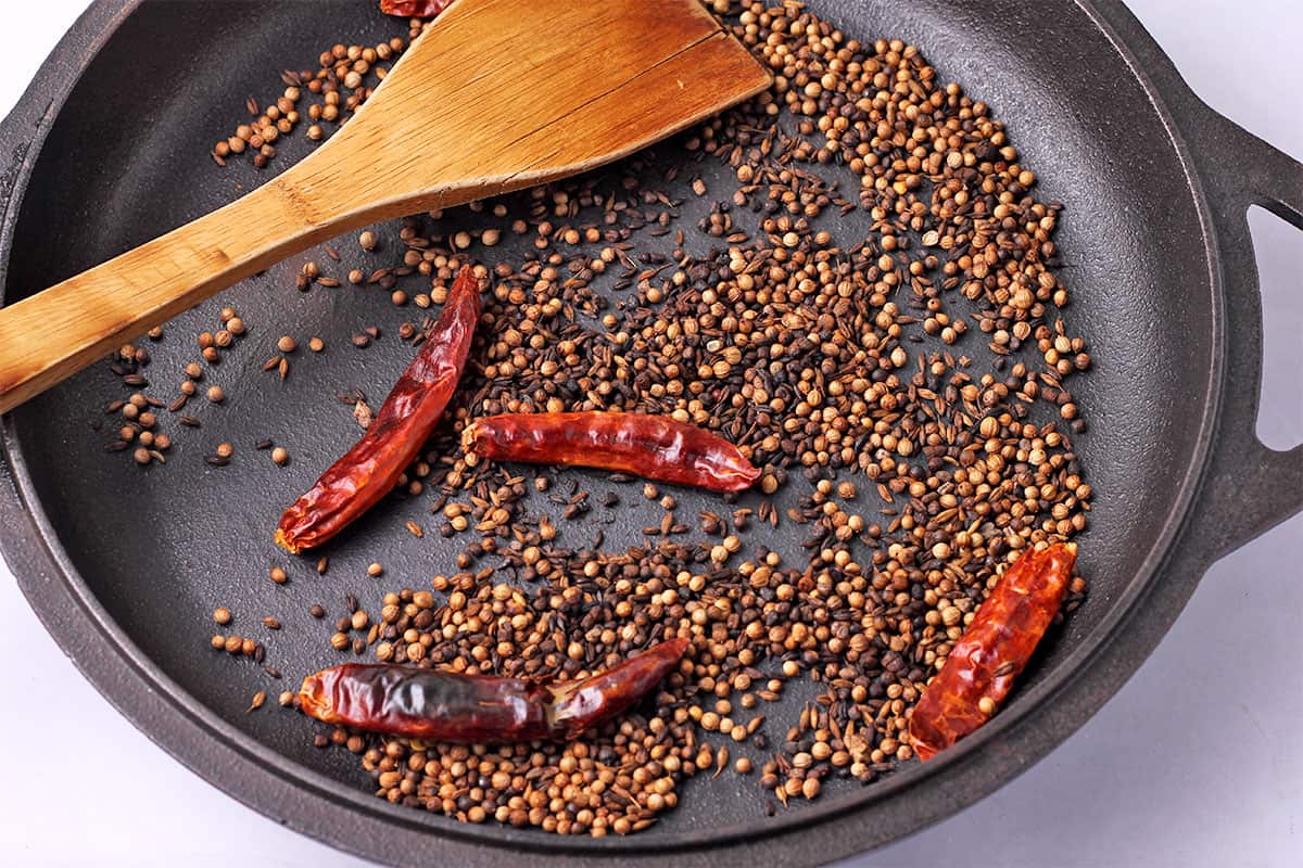 Whole spices and chilies are toasted in a cast iron pan.