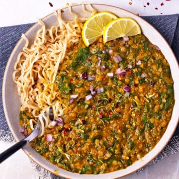 A bowl of spinach and lentil curry over noodles.