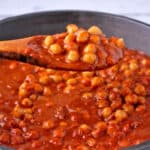 A wooden spoon with chickpea garam masala curry in tomato coconut sauce.