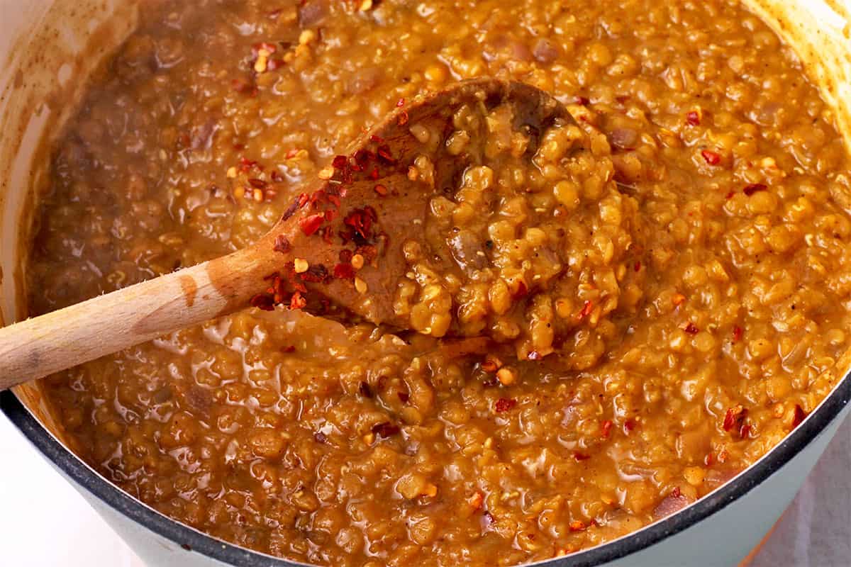 Cooked red lentils in a pot and stirred with a spoon.