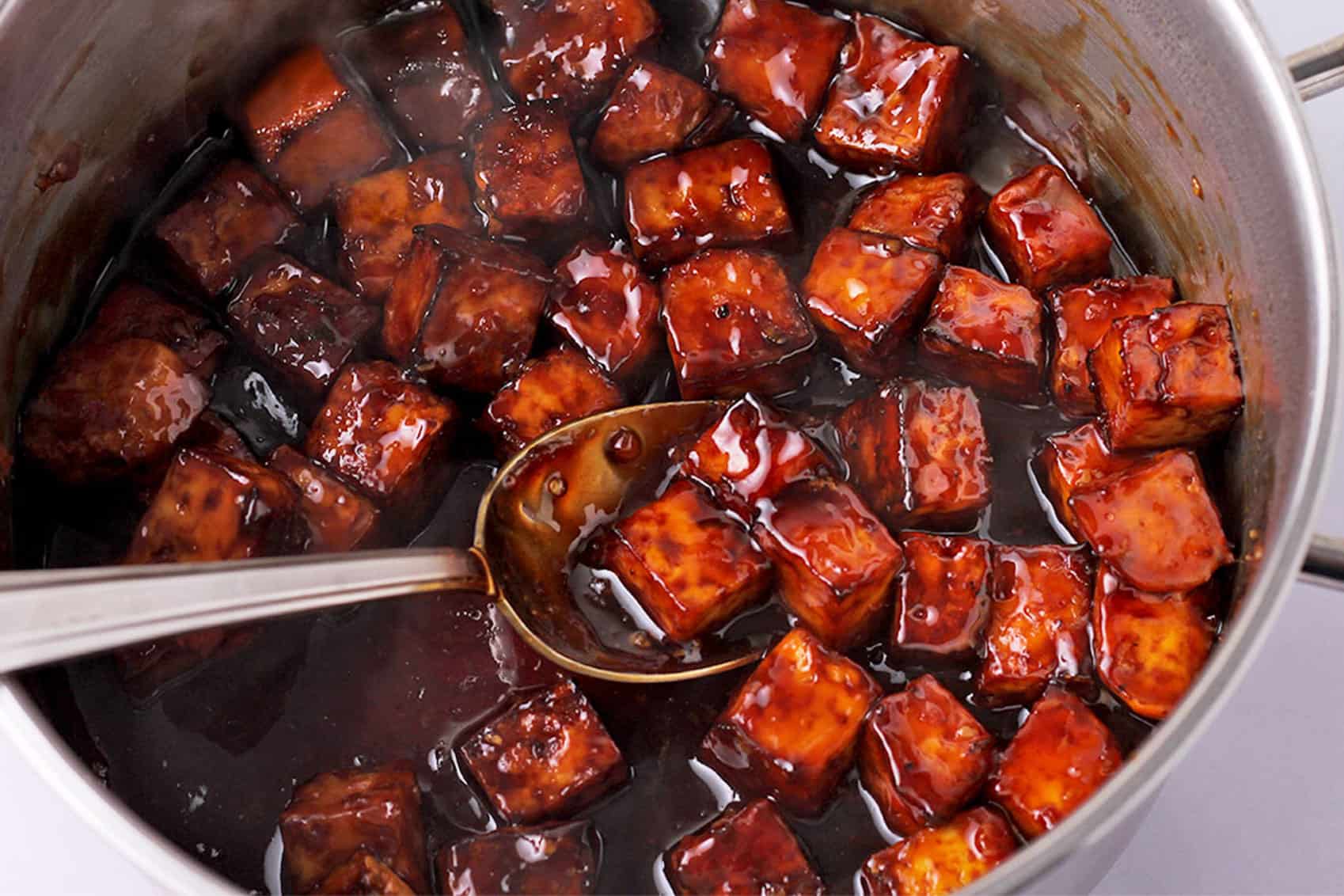 Tofu cubes are mixed with teriyaki sauce in a pan.