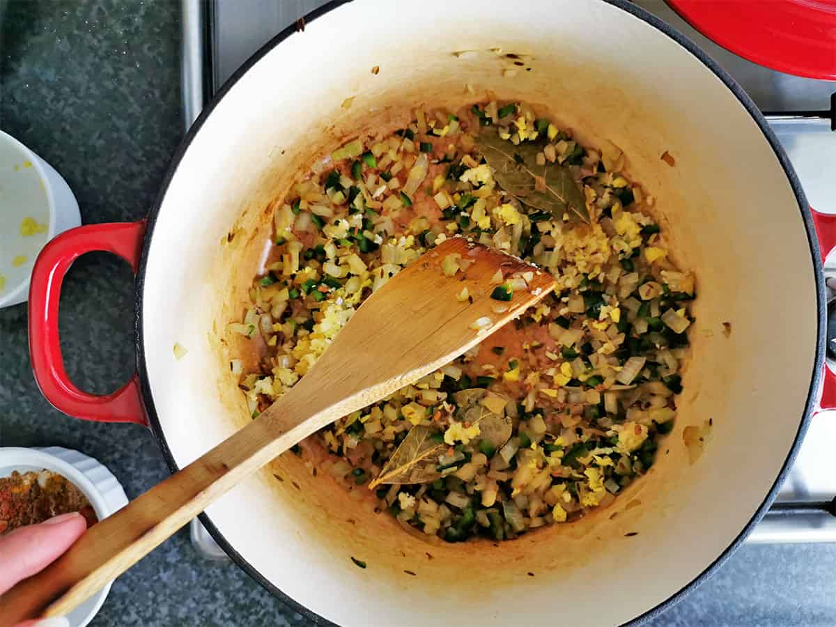 Onions, garlic, ginger, and spices are stirred in a Dutch oven.