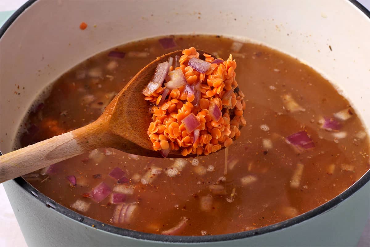 Red onions and split red lentils are stirred into a pot of spices and broth.