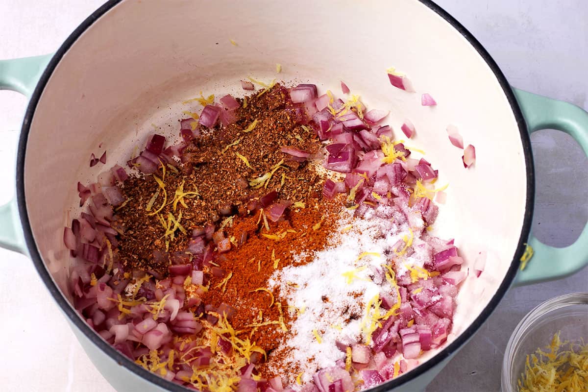 Cooked red onions with lemon zest and spices in a pot.