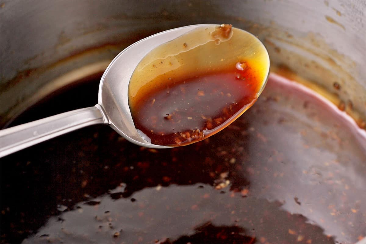 A spoonful of homemade teriyaki sauce is held over a pan of cooking sauce.