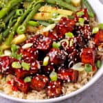 Teriyaki Tofu in a bowl topped with sesame seeds and sliced green onions in a bowl with rice and vegetables.