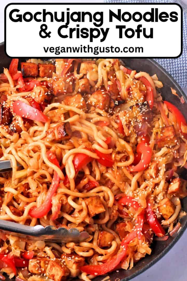 A pan of gochujang noodles with vegetables, tofu, and sesame seeds with text overlay of the recipe title on the photo.