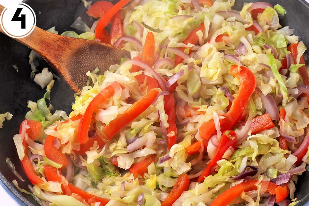 Cooking cabbage, red pepper, and red onions in a skillet.
