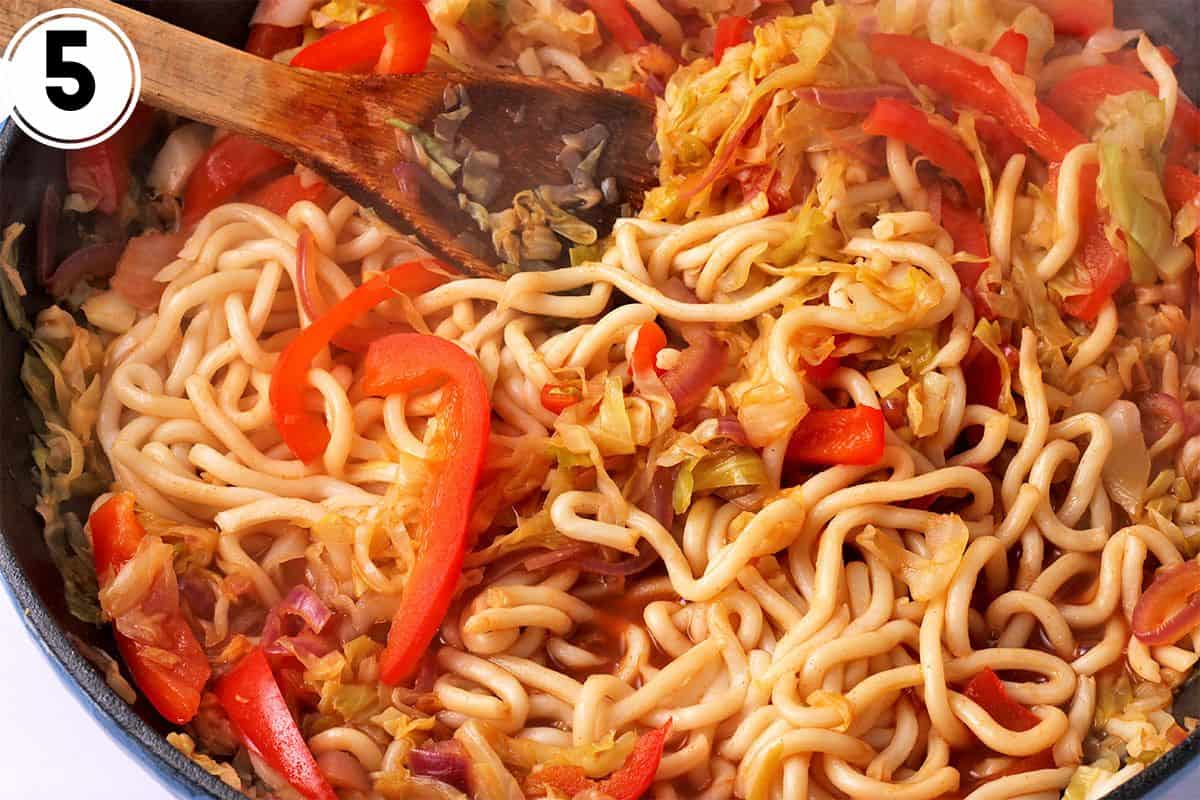 Udon noodles are mixed with cooked cabbage and red peppers.