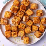 Lemon pepper panko tofu cubes on a white plate with lemon zest.
