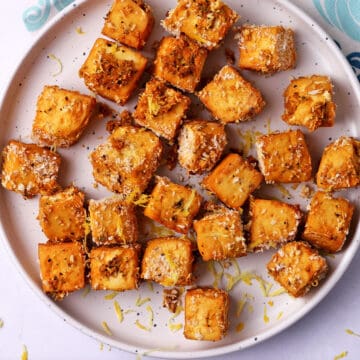 Lemon pepper panko tofu cubes on a white plate with lemon zest.