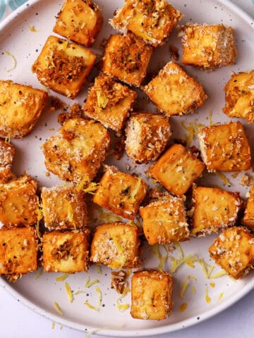 Lemon pepper panko tofu cubes on a white plate with lemon zest.