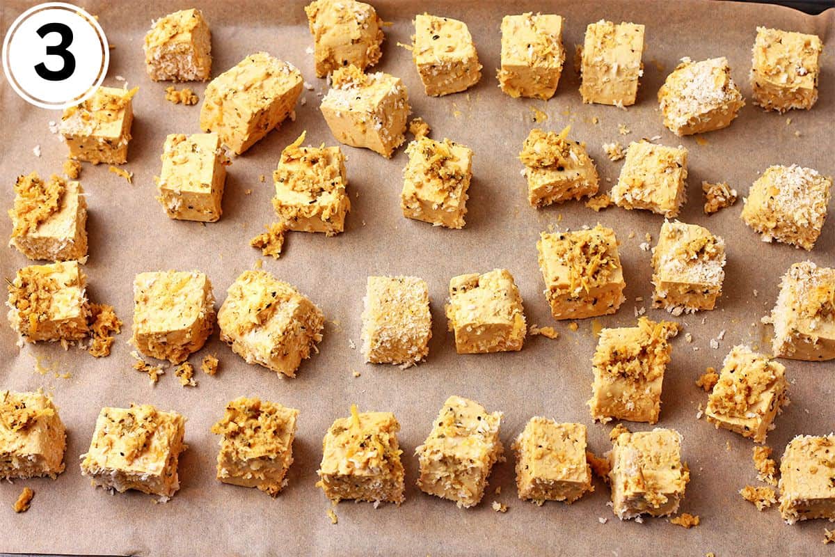 Tofu cubes with panko are arranged on a parchment-lined baking sheet.